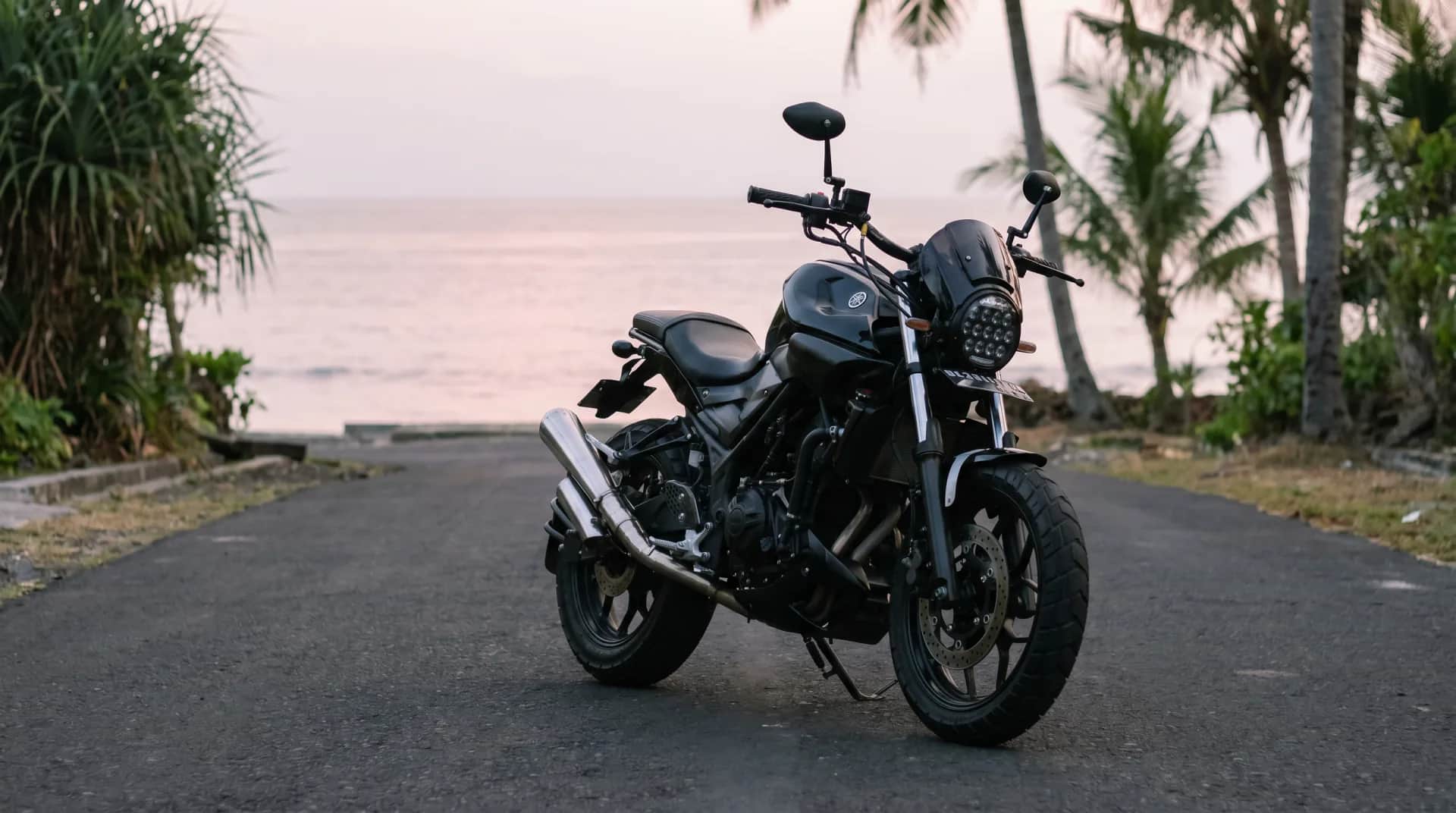 Yamaha MT-25 scrambler on a palm-lined beach road in Bali at dusk