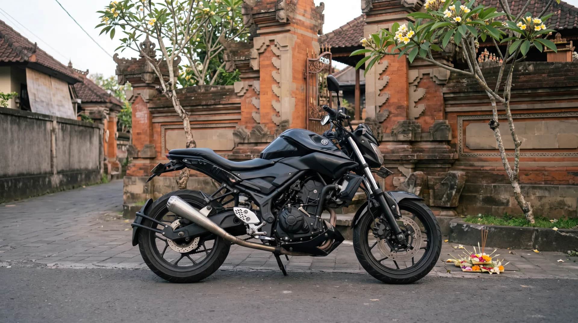Custom Yamaha MT-25 scrambler in a Bali village lane by temple gates and offerings