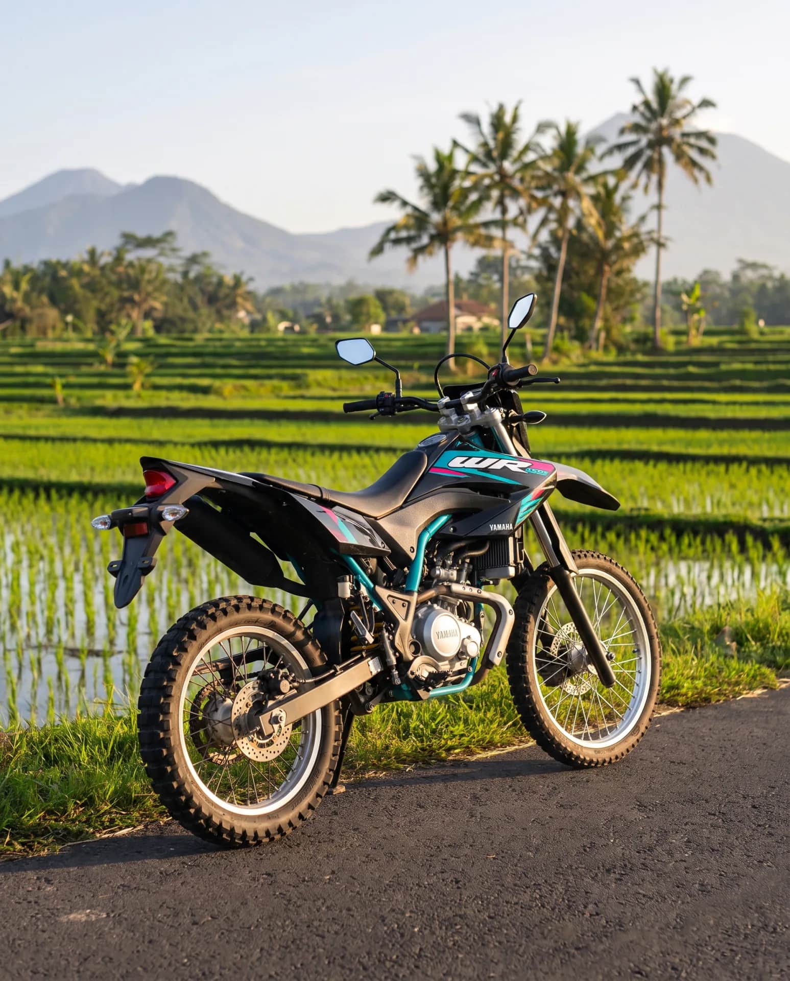 Yamaha WR155 dual-sport parked on a lane beside Bali rice paddies with mountains behind