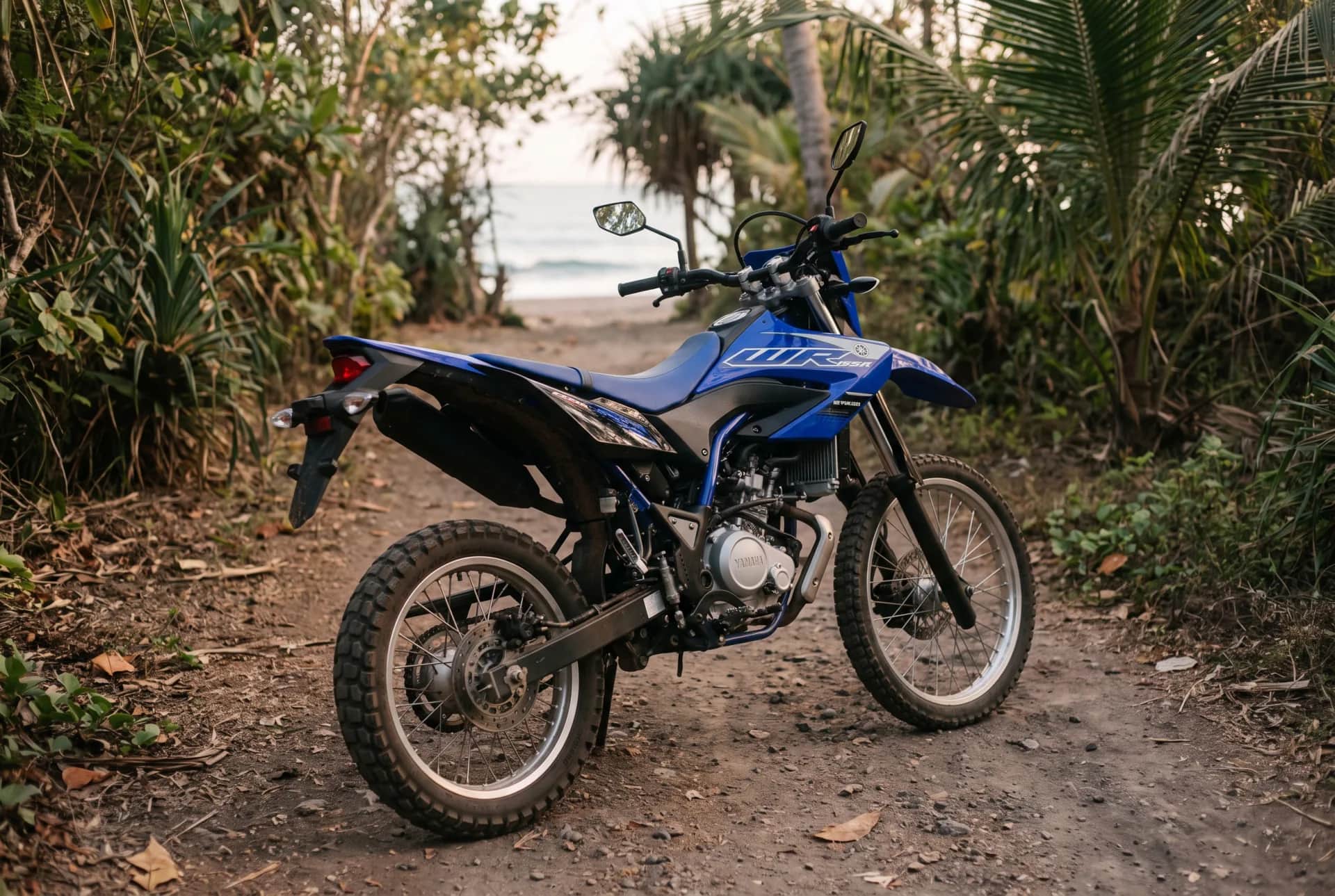 Blue Yamaha WR155 enduro on a dirt path through lush Bali jungle in dappled afternoon light