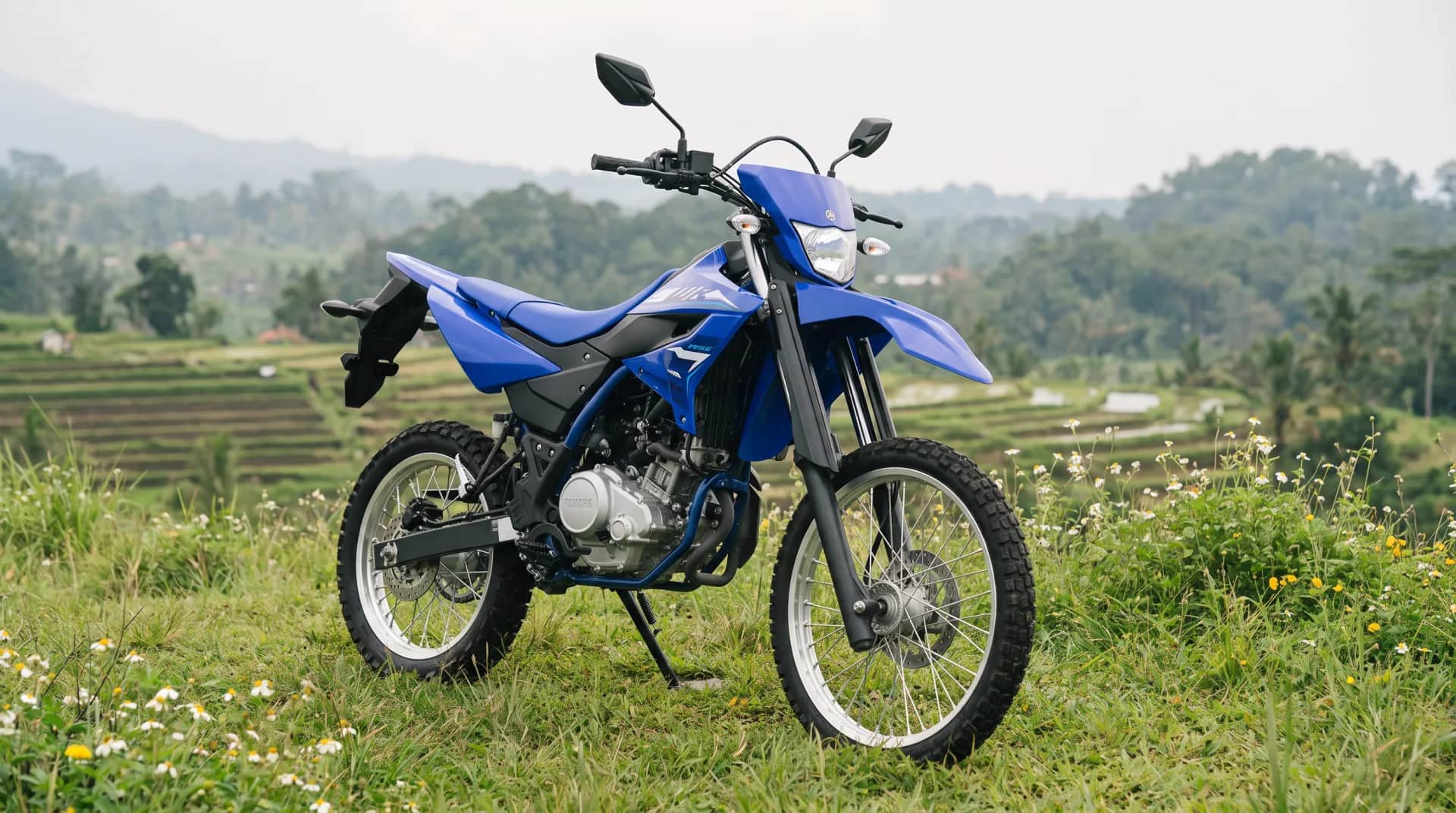 Blue Yamaha WR155 trail motorcycle beside a misty rice paddy terrace in the Bali highlands